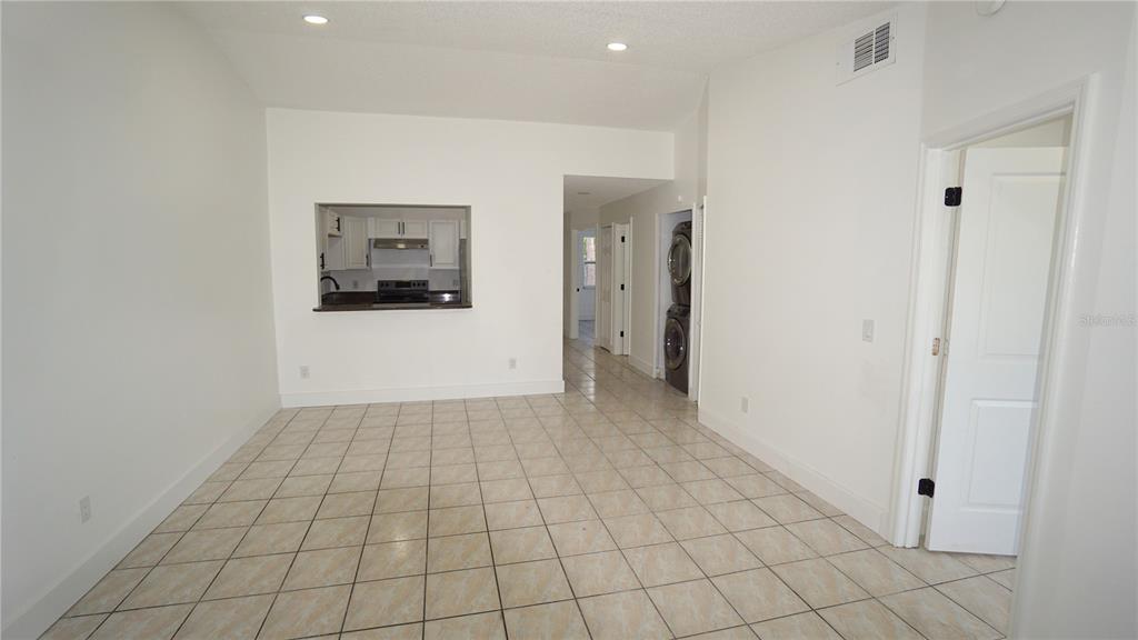 A room with light-colored tile flooring, white walls, a kitchen pass-through, and stacked laundry appliances — 834 ANGELA LANE, KISSIMMEE, FL