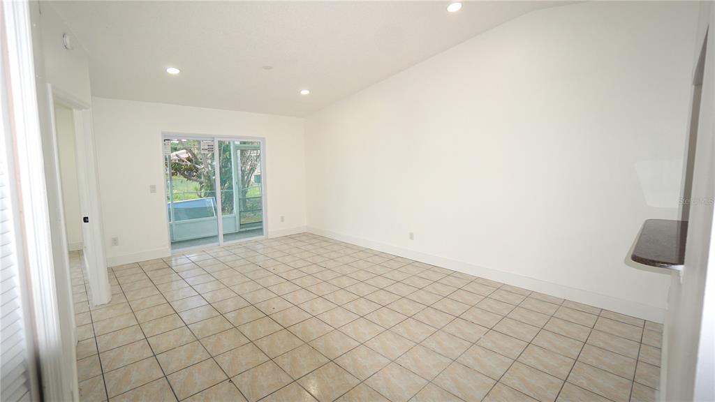 A bright, empty room features light-colored tile flooring, white walls, and a sliding glass door — 834 ANGELA LANE, KISSIMMEE, FL