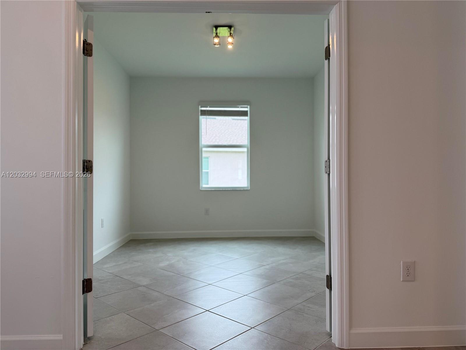 A view through a doorway into an empty room with tile flooring and a window — 20821 Copperhead, Lehigh Acres FL 33936, LEHIGH ACRES, FL