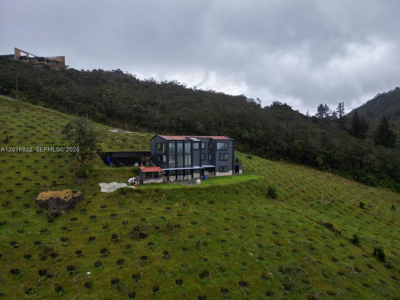 A modern, multi-story dark gray house sits on a grassy hillside under a cloudy sky — CRA 7 #237-04 Bogota, Colombia, FL