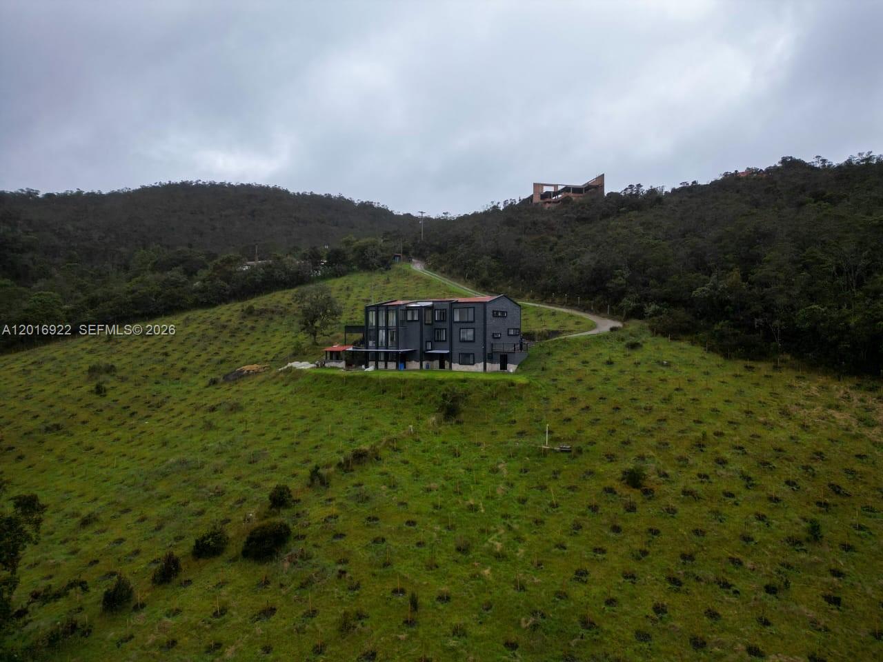 A modern multi-story house sits on a grassy hillside under a cloudy sky — CRA 7 #237-04 Bogota, Colombia, FL