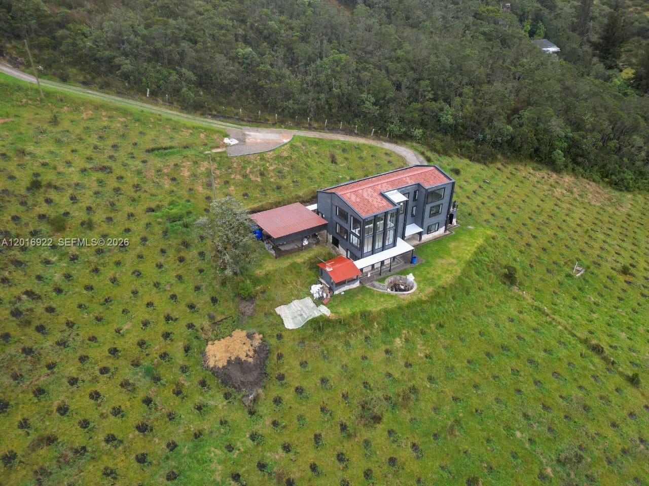 An aerial view shows a modern multi-story house with a red roof on a hillside — CRA 7 #237-04 Bogota, Colombia, FL