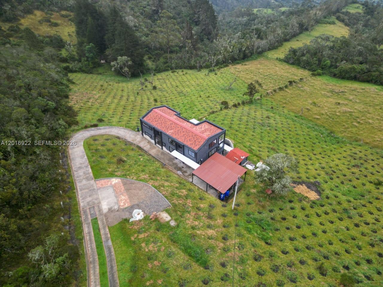 An aerial view shows a modern dark-sided house with a red roof situated on a hillside — CRA 7 #237-04 Bogota, Colombia, FL