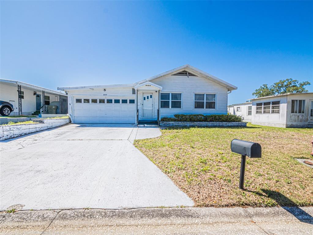 A single-story white house with a garage and a concrete driveway under a blue sky — 2609 HOUSTON PLACE, LEESBURG, FL