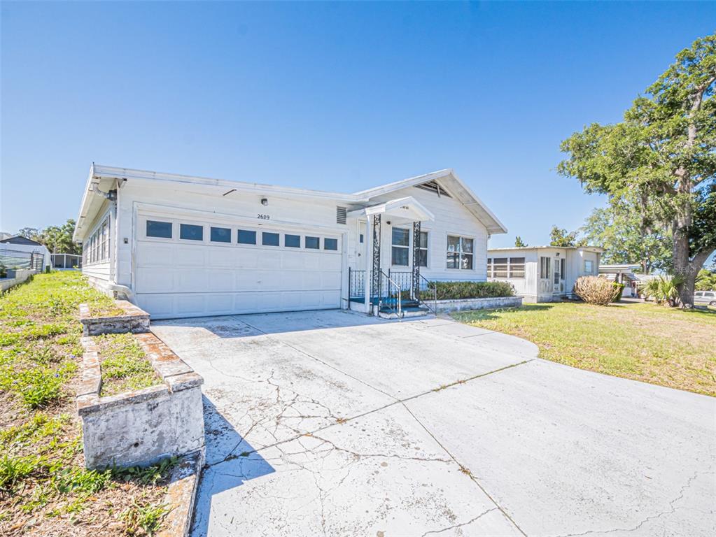 A white single-story house with a garage and a concrete driveway under a blue sky — 2609 HOUSTON PLACE, LEESBURG, FL
