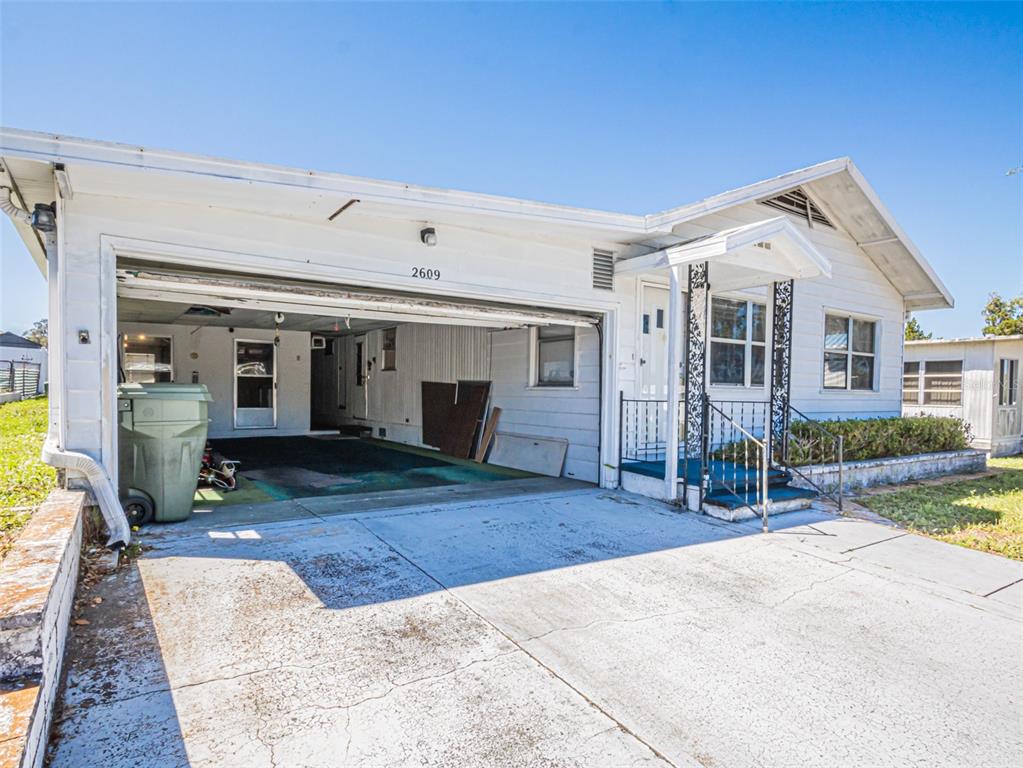 A white single-story house features a large open carport and a small covered front porch — 2609 HOUSTON PLACE, LEESBURG, FL