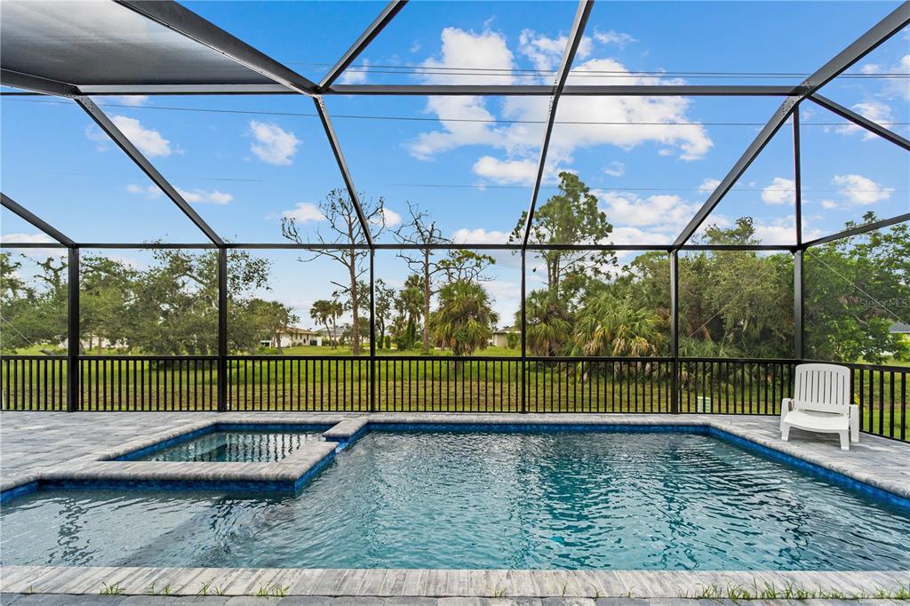 A screened-in pool and spa area with a patio overlooking a grassy yard and trees — 265 ANNAPOLIS LANE, ROTONDA WEST, FL