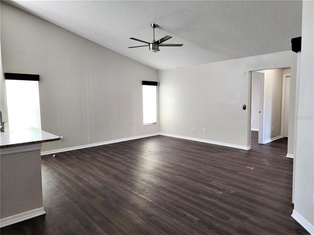 An empty living room features dark wood-look flooring, light gray walls, and a ceiling fan — 13404 IRONTON DRIVE, TAMPA, FL