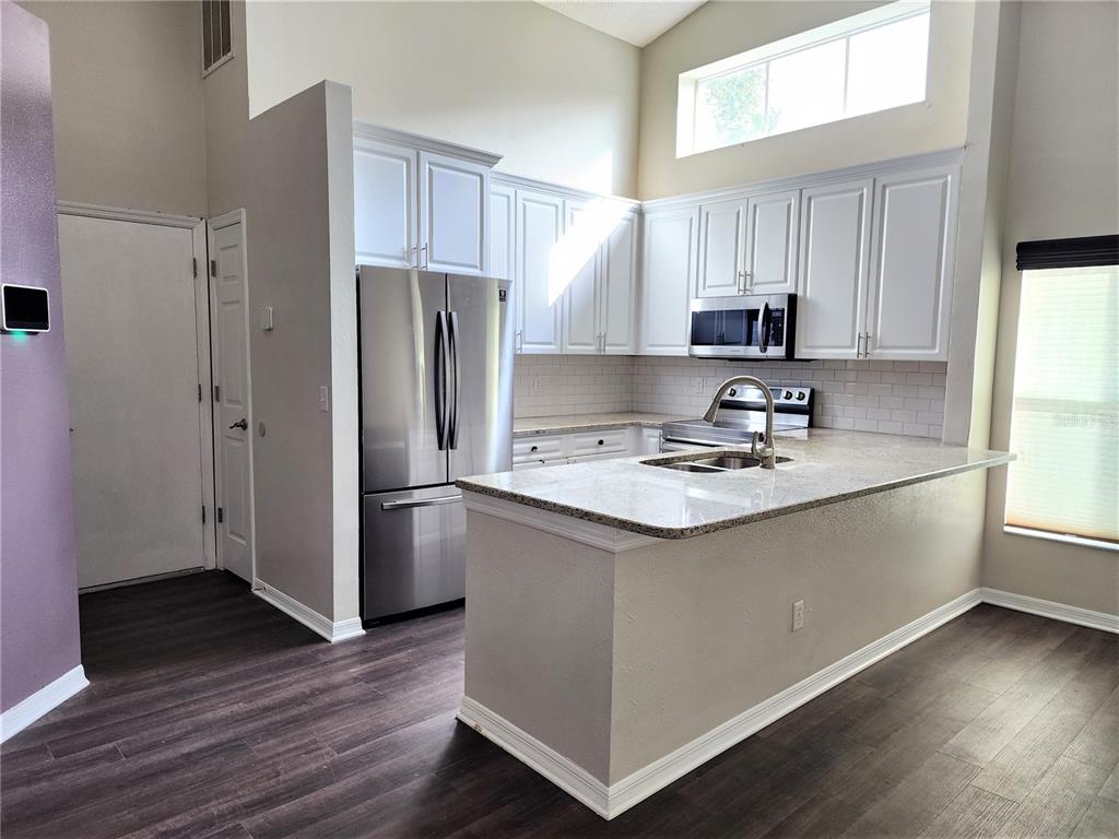 A kitchen features white cabinets, stainless steel appliances, granite countertops, and dark wood-look flooring — 13404 IRONTON DRIVE, TAMPA, FL