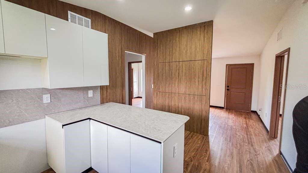A kitchen with white cabinets and a stone-topped island faces a wood-paneled wall — 5620 VIRTUDES STREET, SEBRING, FL