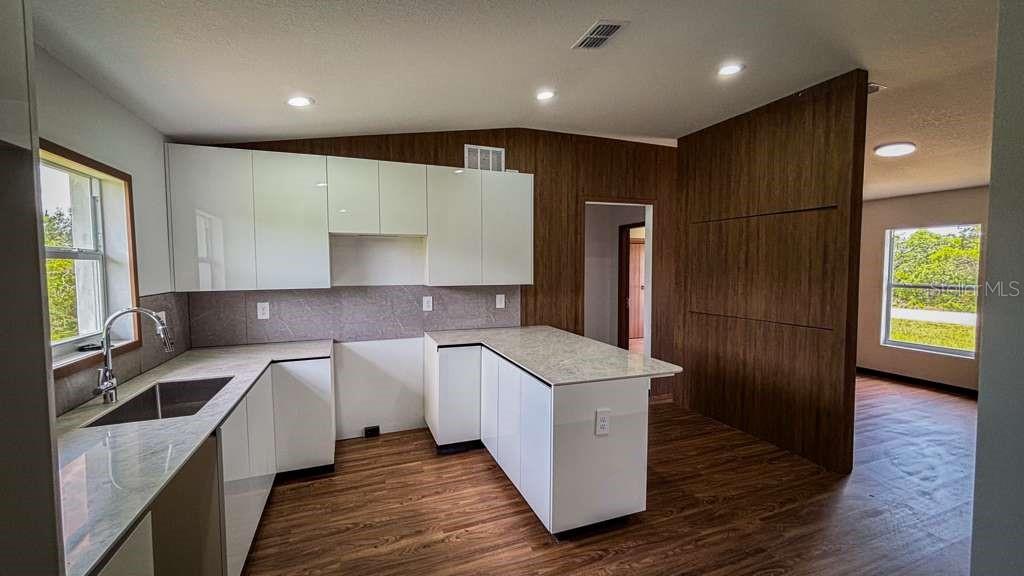 A modern kitchen features white cabinets, stone countertops, and wood-look flooring — 5620 VIRTUDES STREET, SEBRING, FL