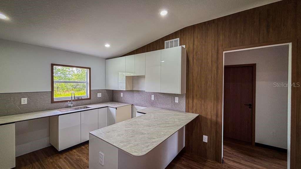 A kitchen features white cabinets, a stone-patterned countertop, and wood-paneled walls — 5620 VIRTUDES STREET, SEBRING, FL