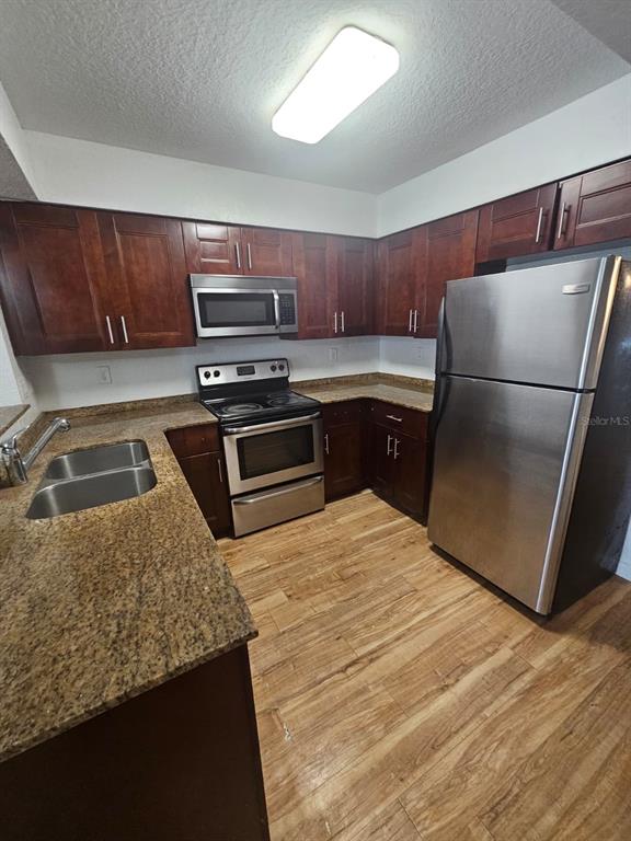 A kitchen features dark wood cabinets, granite countertops, stainless steel appliances, and wood-look flooring — 2323 MCCOY ROAD UNIT 801, ORLANDO, FL
