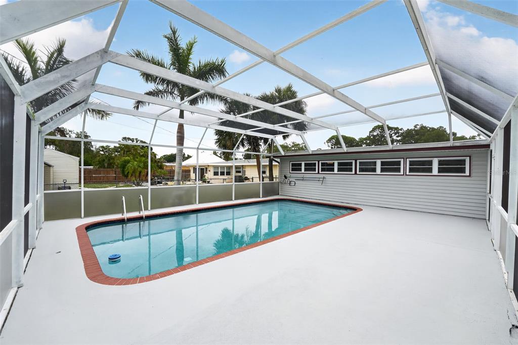 A rectangular swimming pool with a brick border sits inside a screened-in patio enclosure — 2505 WOOD STREET, SARASOTA, FL