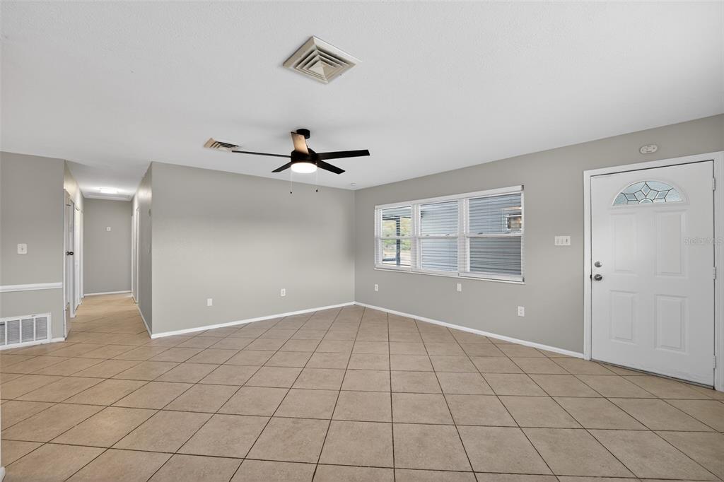 An empty living room features light-colored tile flooring, gray walls, a ceiling fan, and windows — 2505 WOOD STREET, SARASOTA, FL