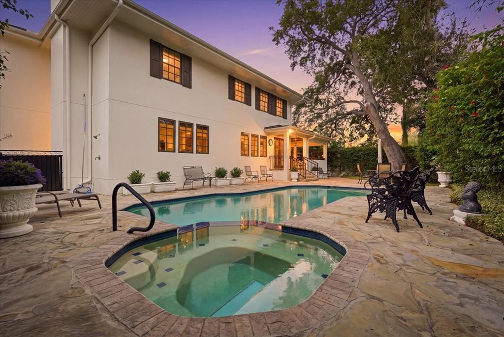 A backyard features a swimming pool, a hot tub, and a stone patio beside a house — 89 MARTINIQUE AVENUE, TAMPA, FL