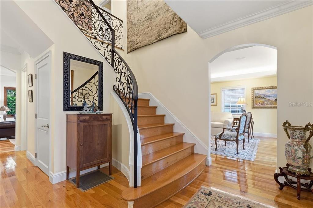 A foyer features a curved wooden staircase with an ornate black metal railing and hardwood floors — 89 MARTINIQUE AVENUE, TAMPA, FL