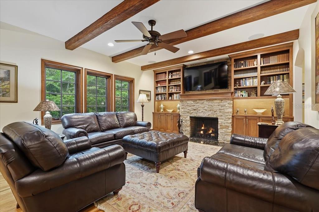 A living room features a stone fireplace, built-in bookshelves, leather furniture, and exposed wood ceiling beams — 89 MARTINIQUE AVENUE, TAMPA, FL