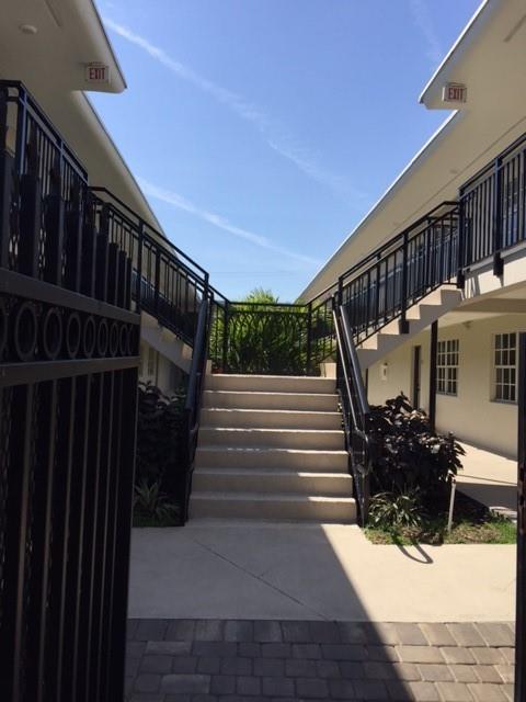 A concrete staircase leads up between two white apartment buildings with black metal railings — NORTH MIAMI BEACH, FL