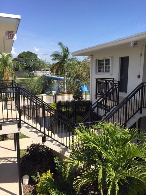 An outdoor staircase with black metal railings leads to a building entrance near palm trees — NORTH MIAMI BEACH, FL
