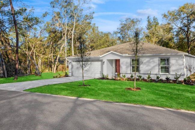 A single-story white house with a two-car garage sits on a grassy lot with trees — 14101 ENGLISH PARROT ROAD, WEEKI WACHEE, FL