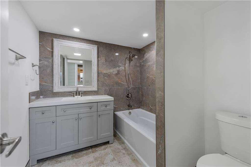 A bathroom features a grey vanity, a white bathtub, and brown stone-look wall tiles — 7080 Environ Boulevard # 522, Lauderhill FL 33319, LAUDERHILL, FL