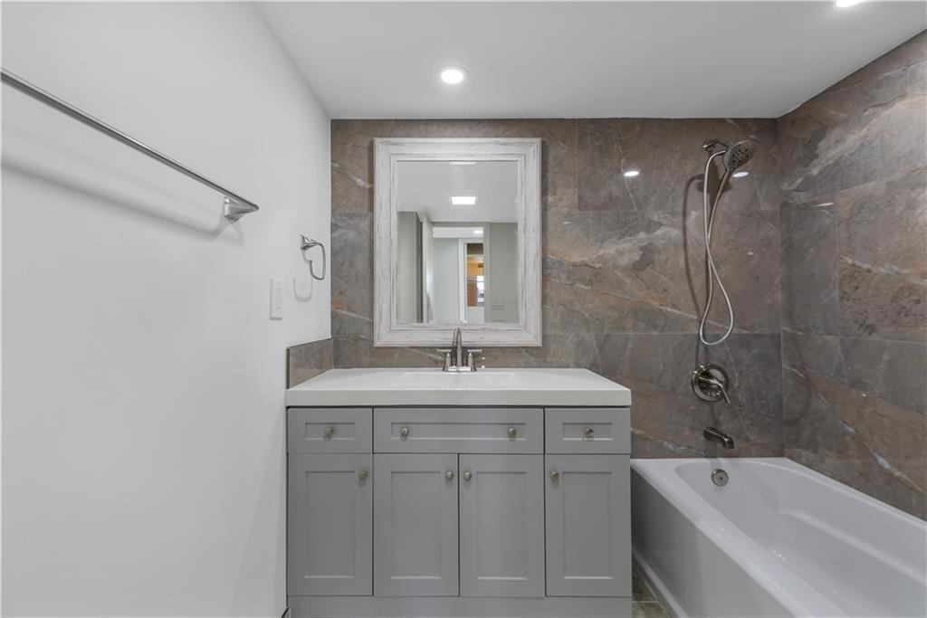 A bathroom features a gray vanity, a white tub, and brown stone-look wall tiles — 7080 Environ Boulevard # 522, Lauderhill FL 33319, LAUDERHILL, FL