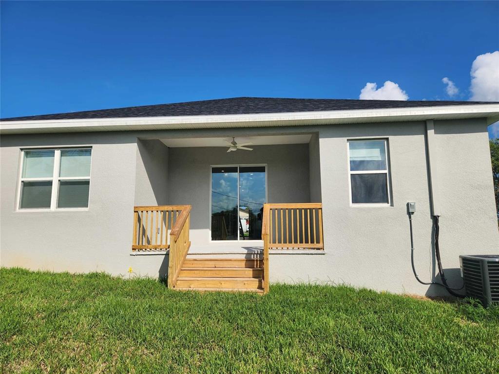 The exterior rear view of a house features a covered patio with wooden steps — 6514 GRAPEWOOD ROAD, SPRING HILL, FL