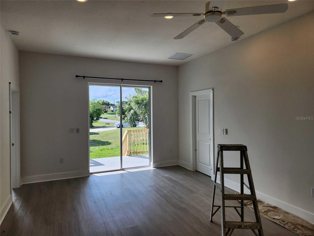 An empty room features light wood-look flooring, a ceiling fan, and sliding glass doors — 6514 GRAPEWOOD ROAD, SPRING HILL, FL