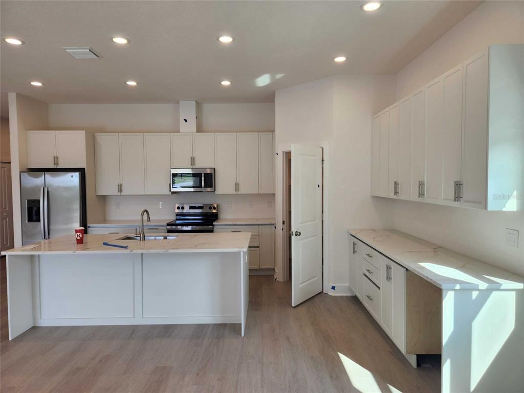 A modern kitchen features white cabinetry, a large island with a sink, and light flooring — 6514 GRAPEWOOD ROAD, SPRING HILL, FL