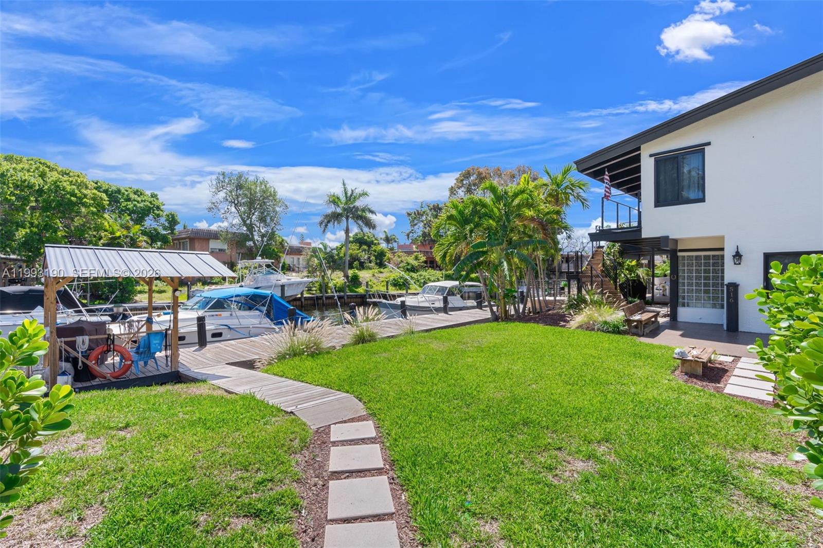 A grassy backyard features a wooden dock, boat slips, and a two-story white house — 516 NE 6th Ave, Deerfield Beach FL 33441, DEERFIELD BEACH, FL