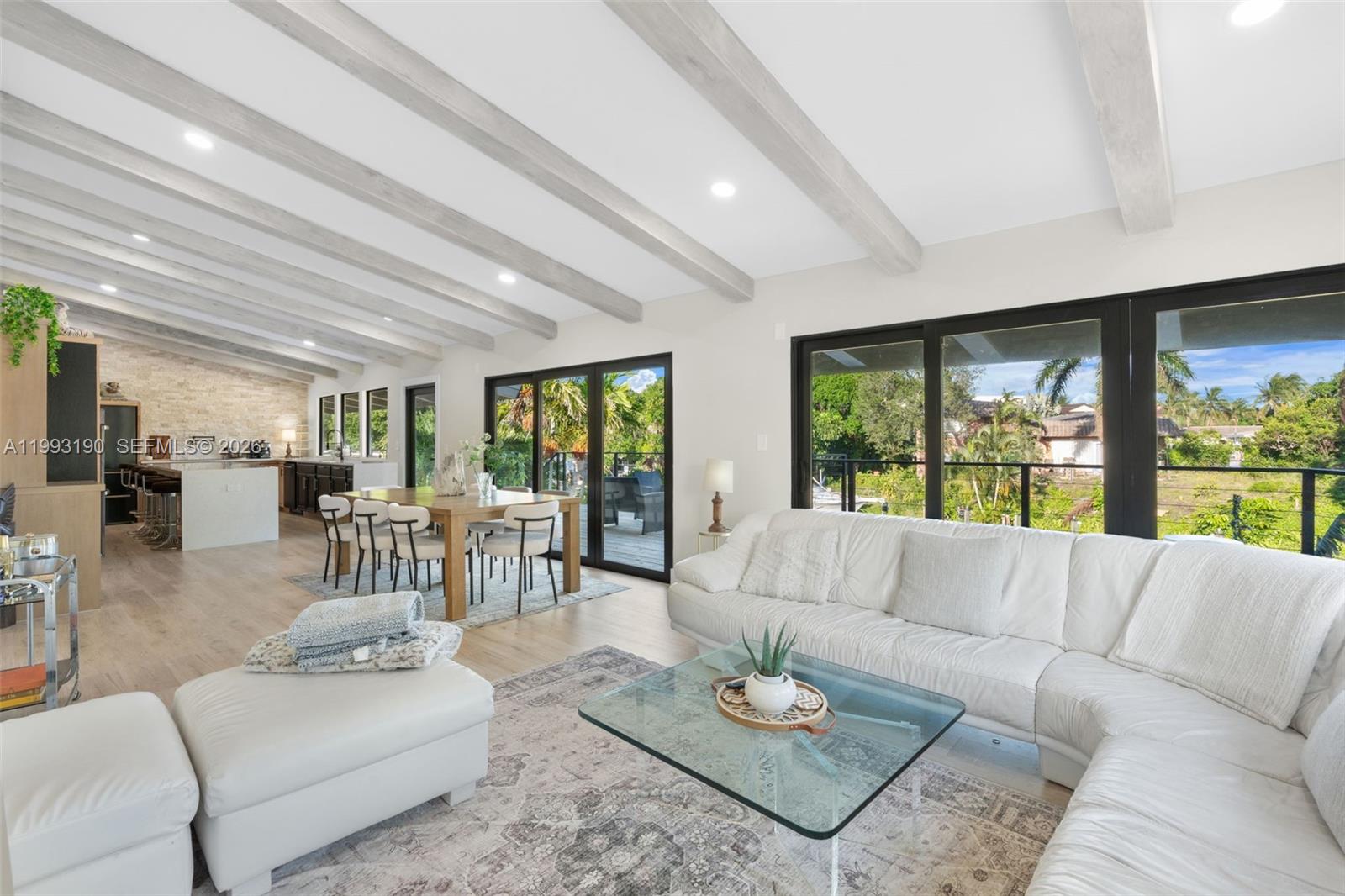 An open-concept living and dining area features vaulted beamed ceilings and large sliding glass doors — 516 NE 6th Ave, Deerfield Beach FL 33441, DEERFIELD BEACH, FL