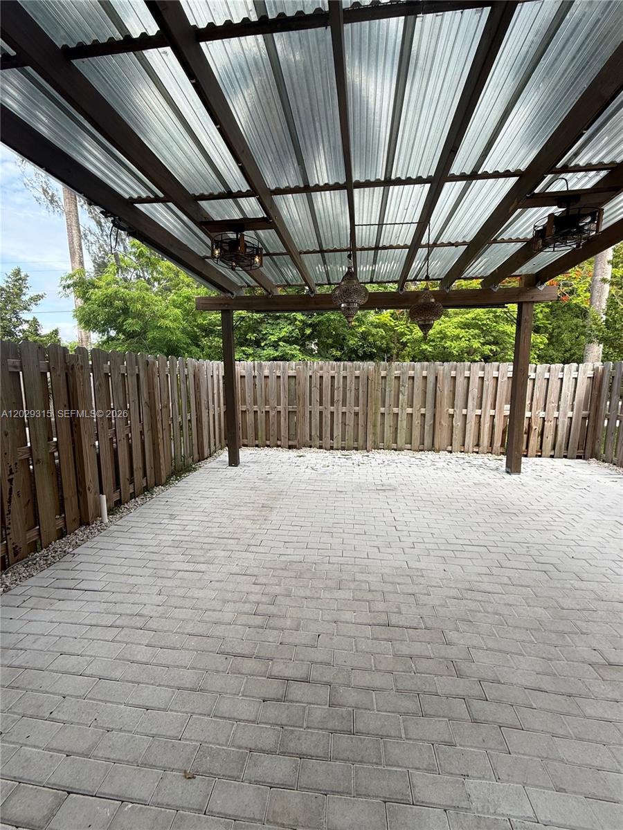 A paved patio area features a wooden pergola with hanging lights and a wooden fence — 24600 SW 119th Pl # 0, Miami FL 33032, MIAMI, FL