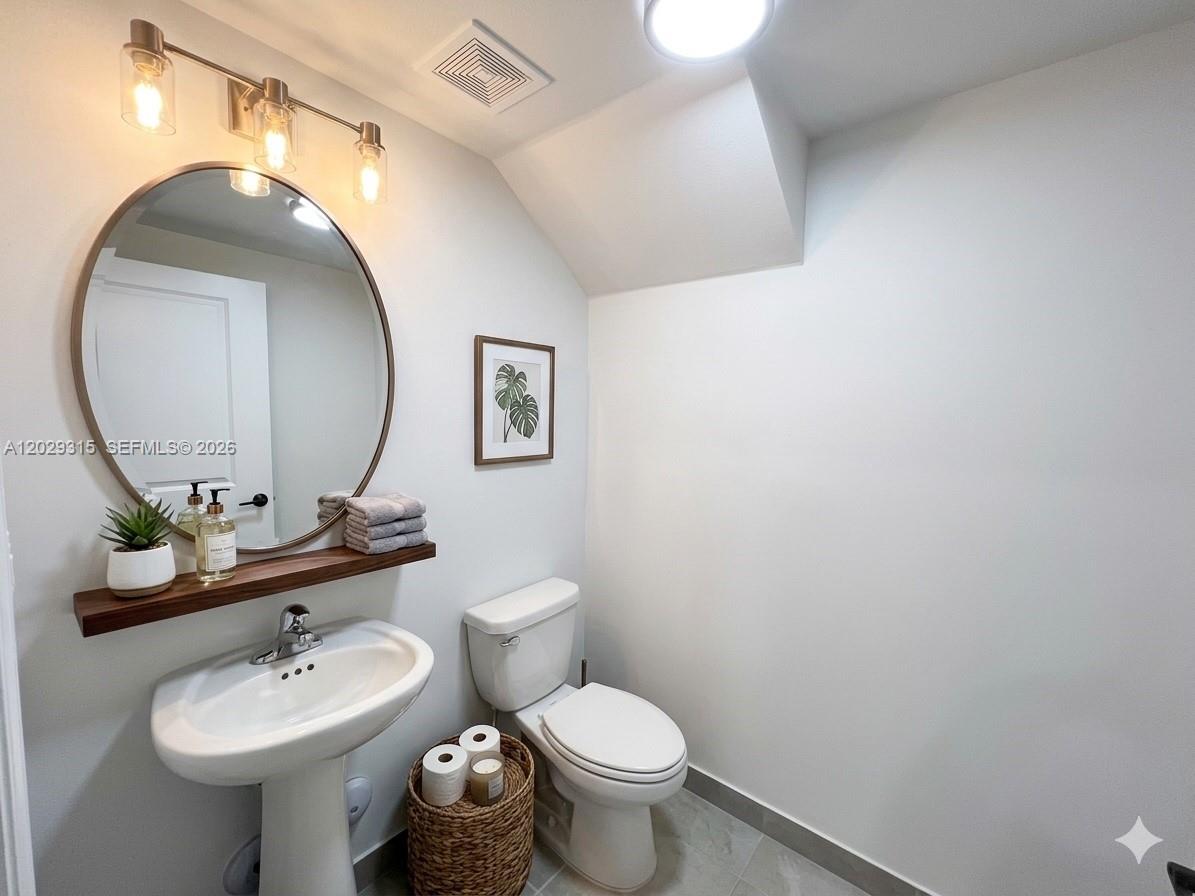 A small bathroom features a pedestal sink, a round mirror, and a toilet — 24600 SW 119th Pl # 0, Miami FL 33032, MIAMI, FL