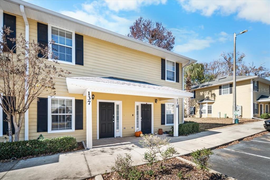 A two-story yellow townhouse exterior features a covered entryway with two black front doors — 2945 SW 35TH PLACE UNIT 137, GAINESVILLE, FL