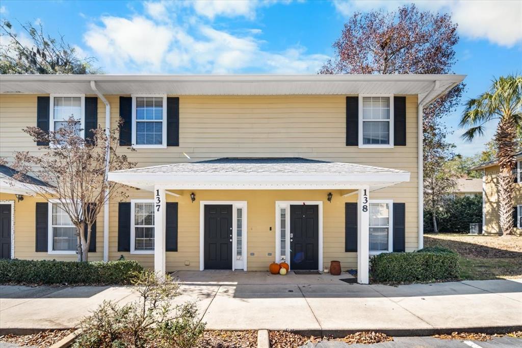 A two-story yellow townhouse exterior features two black front doors and a shared porch — 2945 SW 35TH PLACE UNIT 137, GAINESVILLE, FL