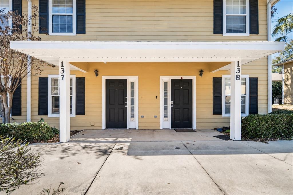 The exterior of a two-story yellow building features two black front doors under a porch — 2945 SW 35TH PLACE UNIT 137, GAINESVILLE, FL