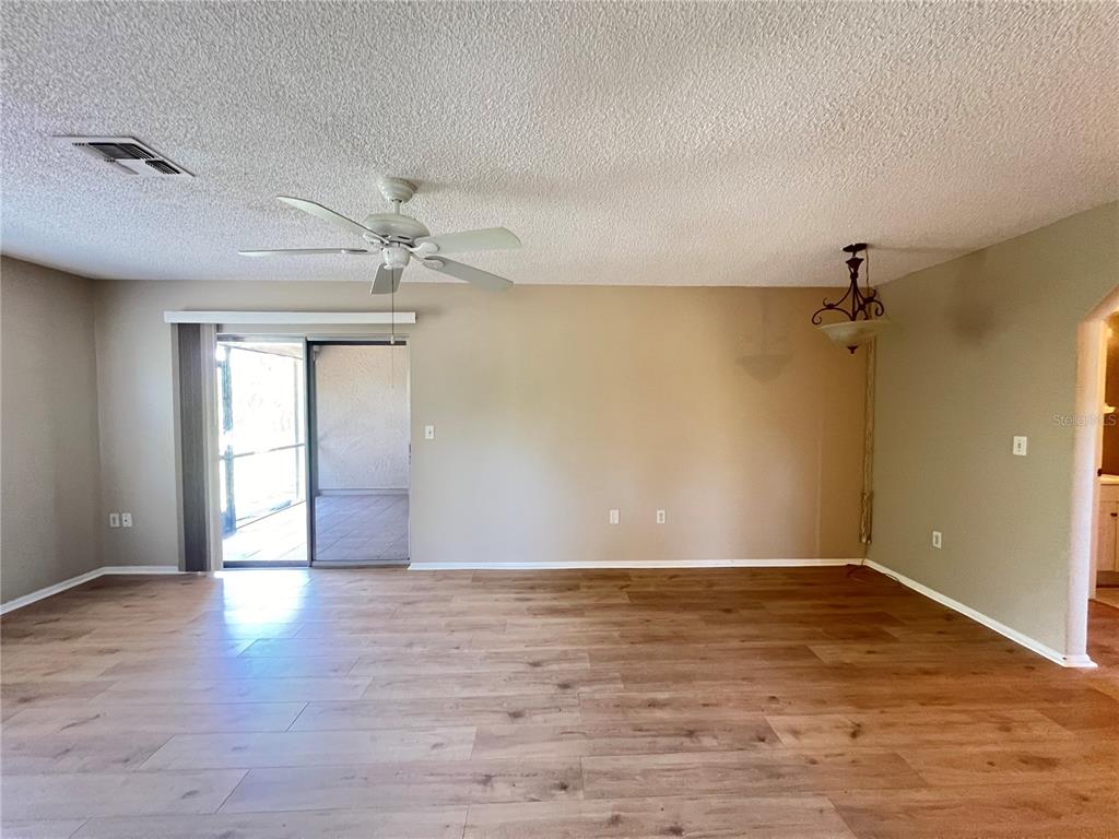 A living room with wood-look flooring, a ceiling fan, and sliding glass doors to a patio — 25068 HARBORVIEW ROAD UNIT 1A, PUNTA GORDA, FL