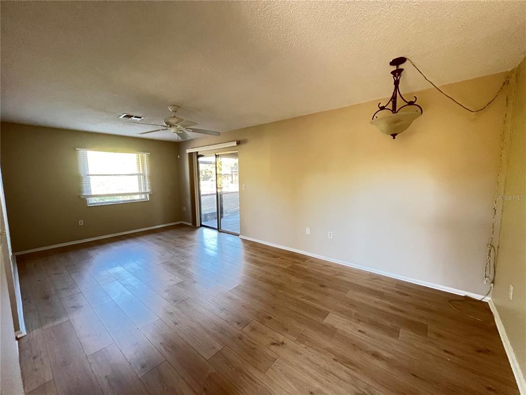 An empty living room features wood-look flooring, a ceiling fan, and sliding glass patio doors — 25068 HARBORVIEW ROAD UNIT 1A, PUNTA GORDA, FL