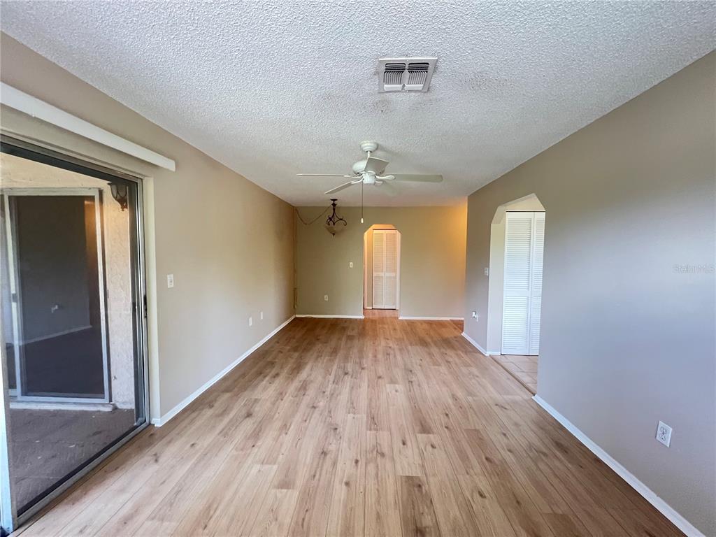 An empty room features light wood-look flooring, a ceiling fan, and a sliding glass door — 25068 HARBORVIEW ROAD UNIT 1A, PUNTA GORDA, FL