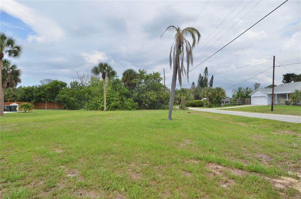 A grassy vacant lot features several palm trees and a view of a nearby house — 610 COQUINA COURT, NOKOMIS, FL