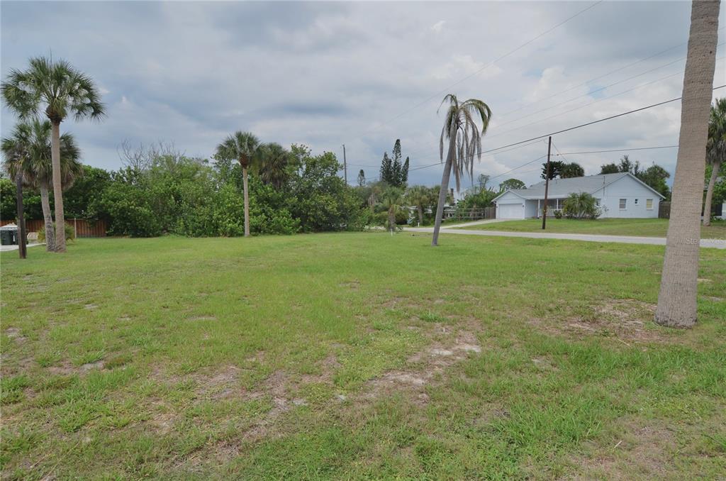 A grassy vacant lot features several palm trees under a cloudy sky near a house — 610 COQUINA COURT, NOKOMIS, FL