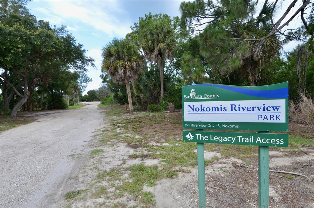 A sign for Nokomis Riverview Park stands beside a dirt road lined with trees — 610 COQUINA COURT, NOKOMIS, FL