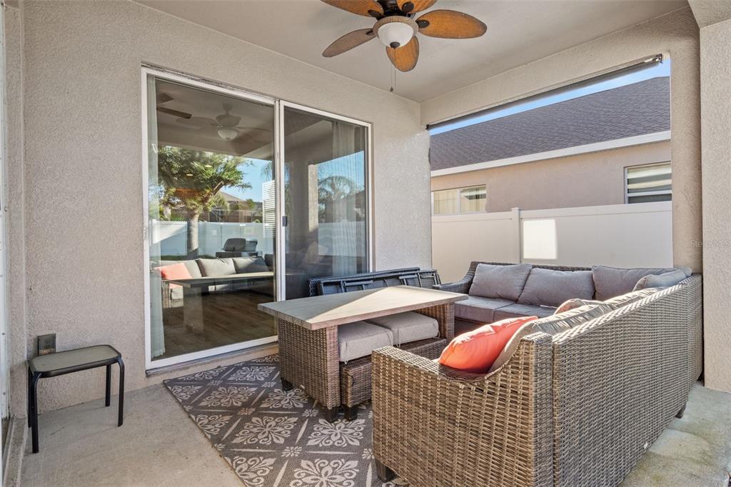 A covered patio features a wicker sectional sofa, a dining table, and a ceiling fan — 19419 RED SKY COURT, LAND O LAKES, FL