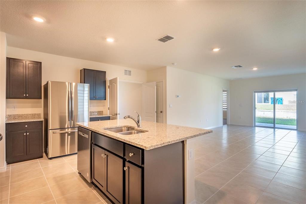 A kitchen with dark cabinets, granite countertops, and stainless steel appliances opens to a living area — 2464 RIBBON FALL AVENUE, DAVENPORT, FL