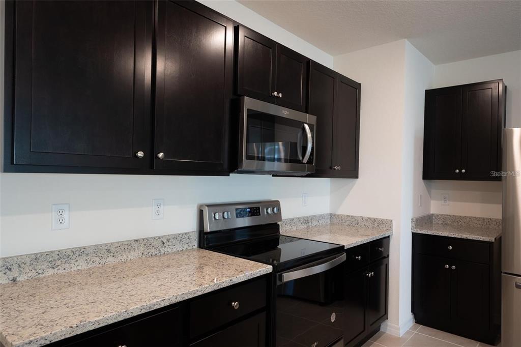 A kitchen features dark wood cabinets, granite countertops, and stainless steel appliances — 2464 RIBBON FALL AVENUE, DAVENPORT, FL