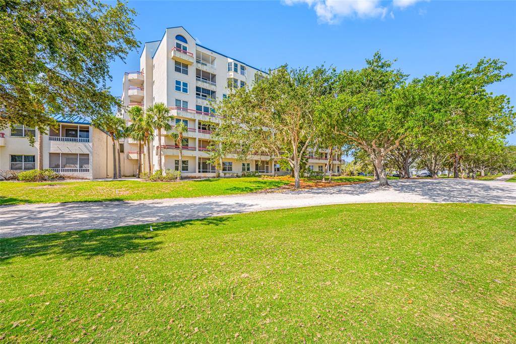 A multi-story apartment building stands behind a large grassy lawn and several mature trees — 2333 FEATHER SOUND DRIVE UNIT A107, CLEARWATER, FL