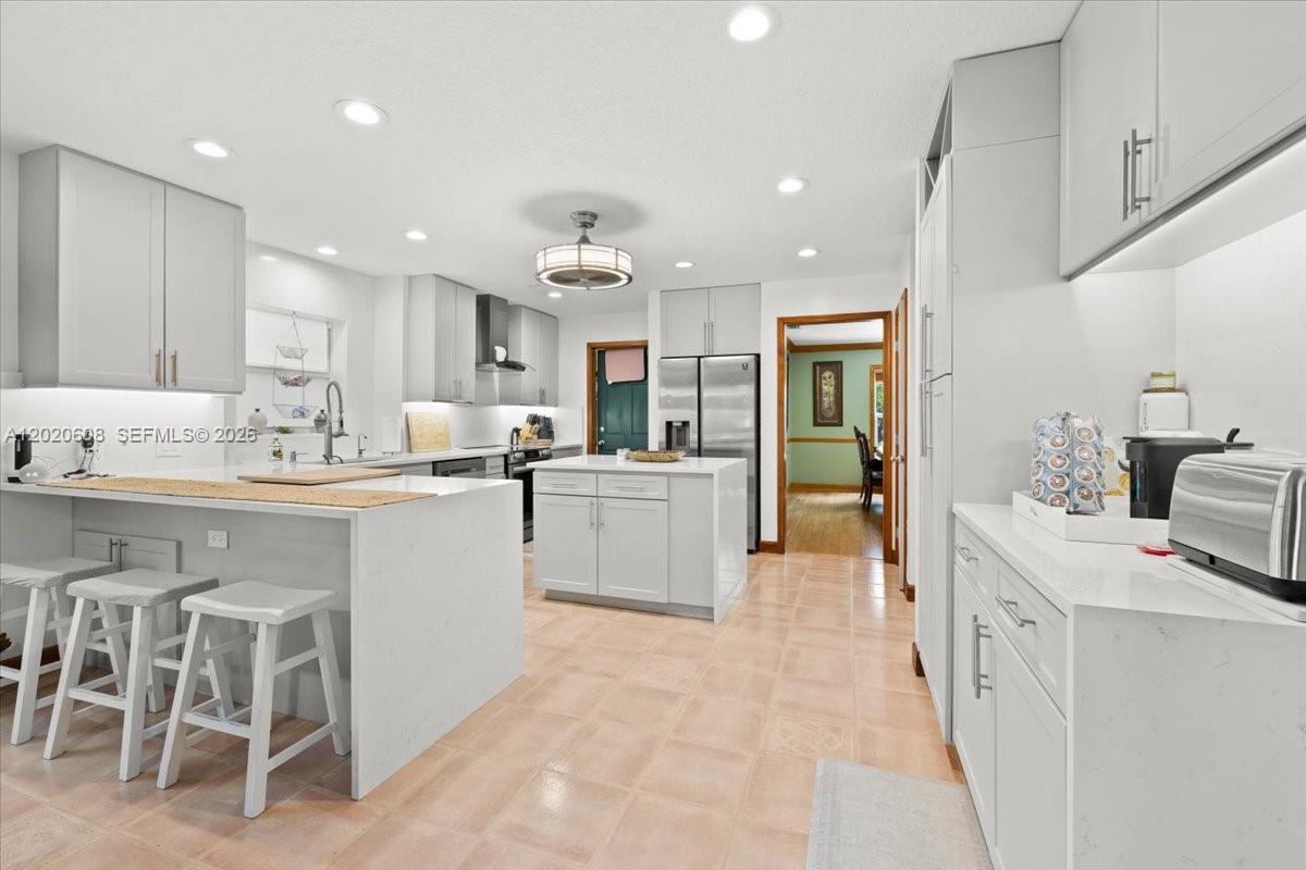 A modern kitchen features white cabinetry, quartz countertops, a central island, and tiled flooring — 10767 N 153rd Ct N, Jupiter FL 33478, JUPITER, FL