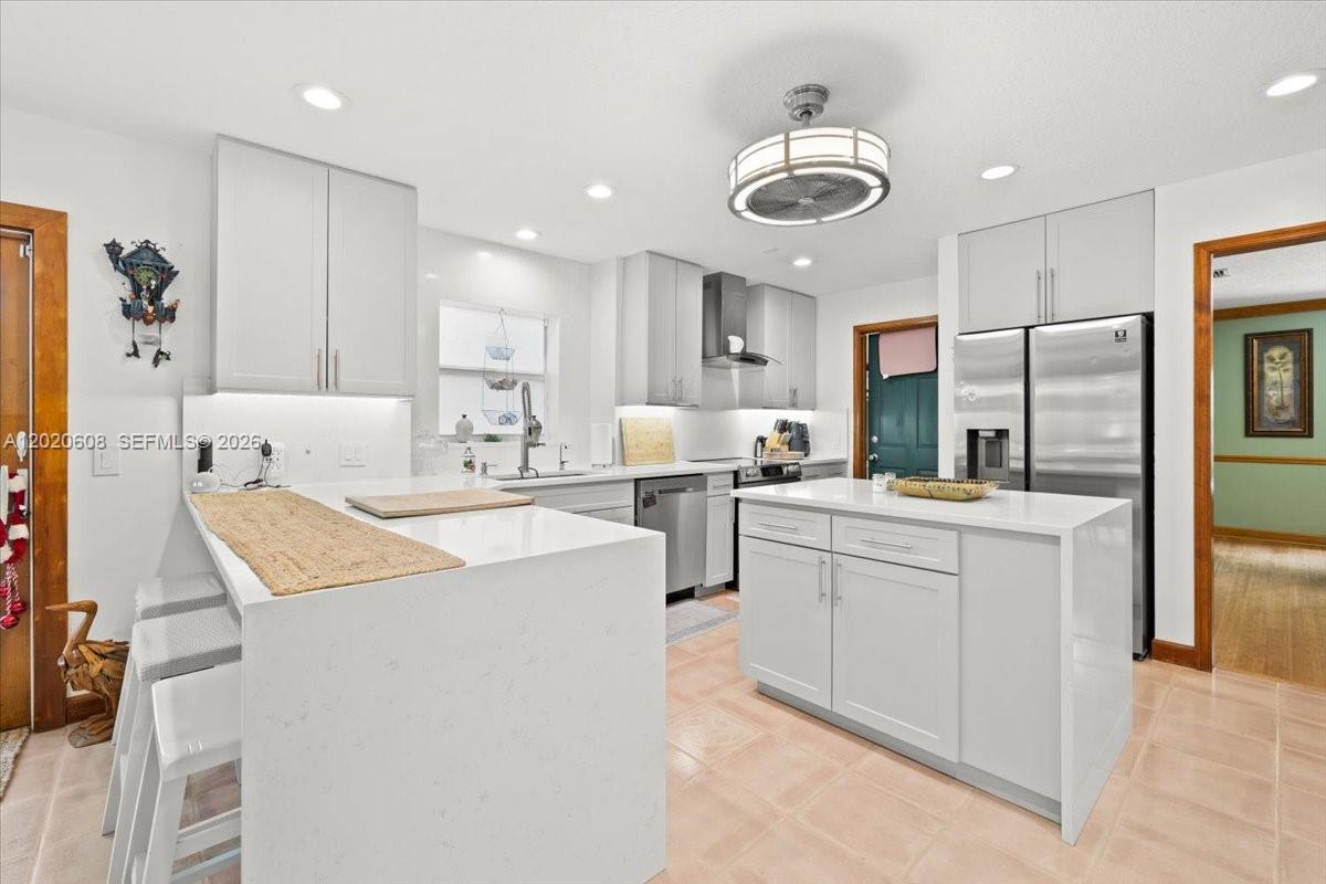 A modern kitchen features white cabinetry, a central island, and stainless steel appliances — 10767 N 153rd Ct N, Jupiter FL 33478, JUPITER, FL