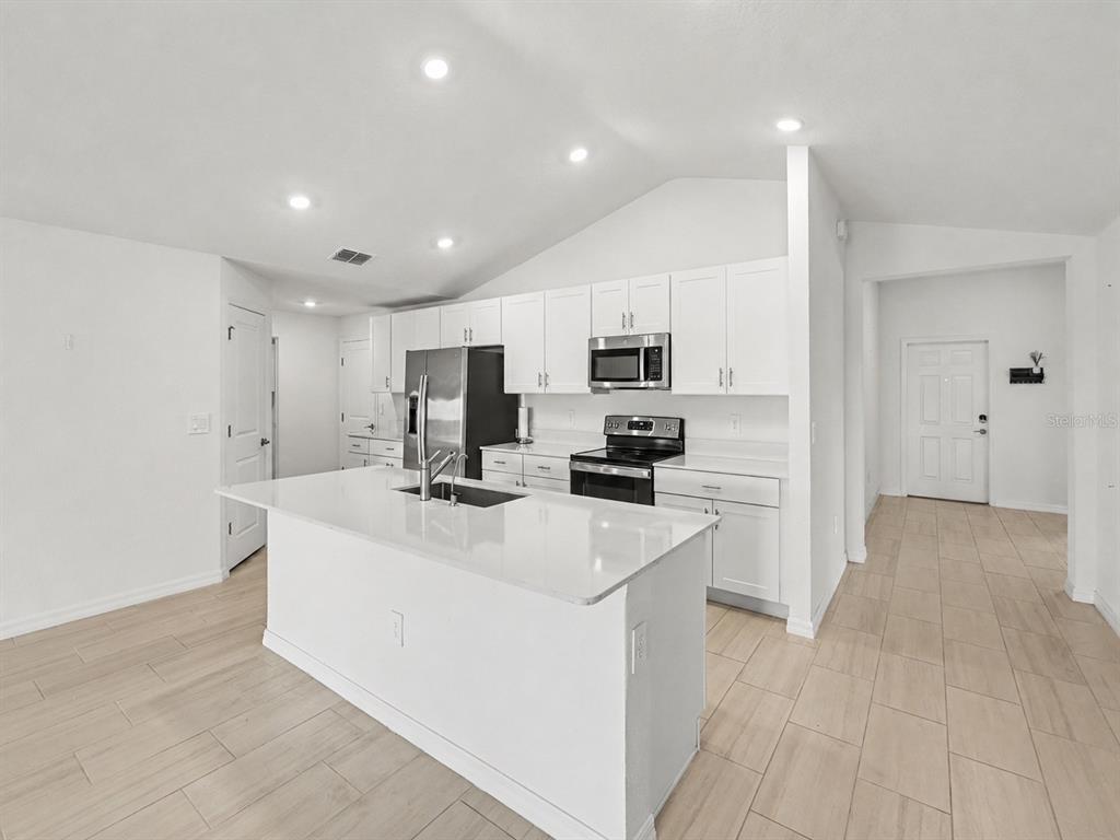 A modern kitchen features white cabinets, stainless steel appliances, a center island, and light flooring — 15281 ZIRCON RED DRIVE, WIMAUMA, FL